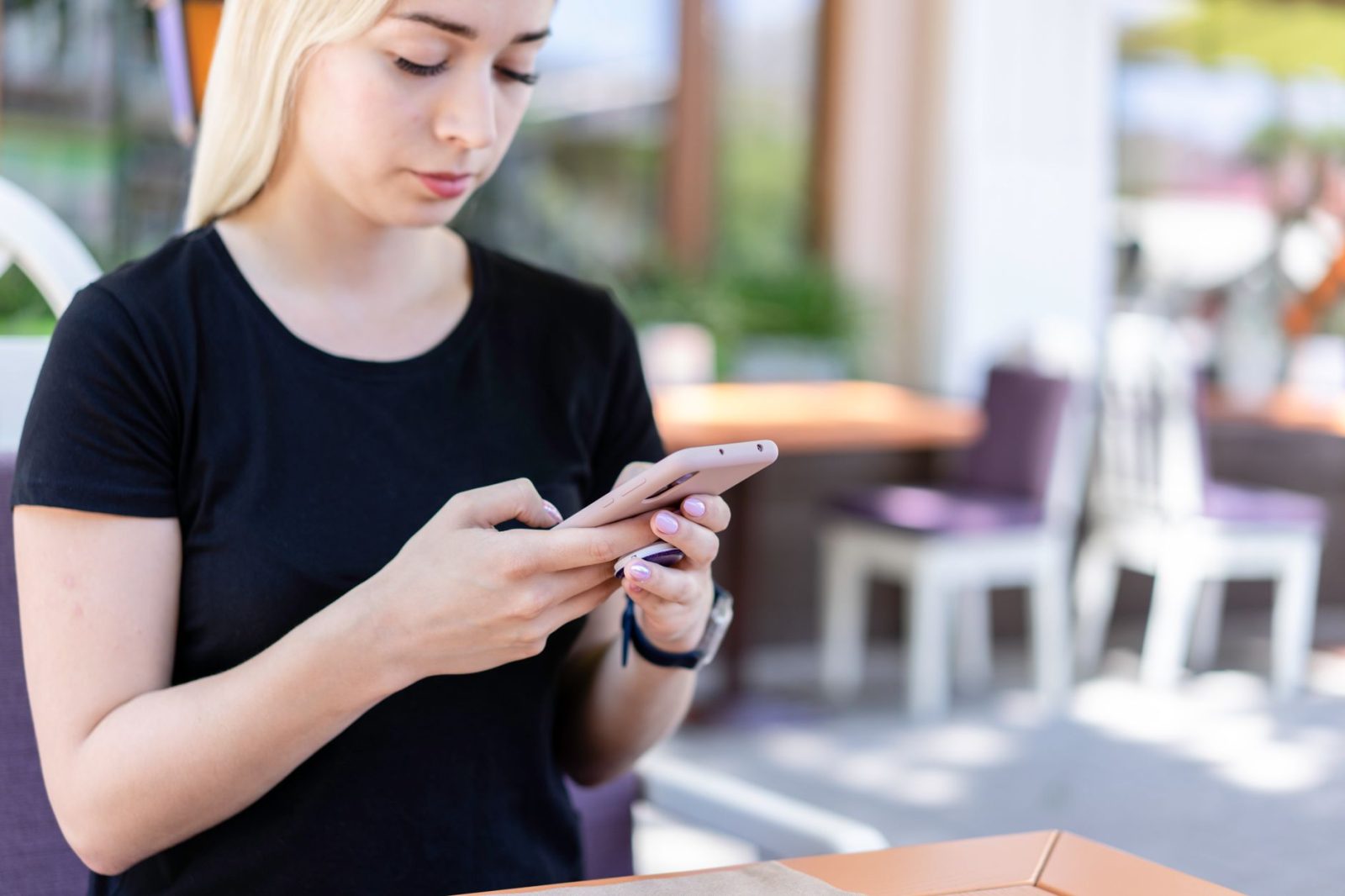A young woman using her phone at an outdoor café table
