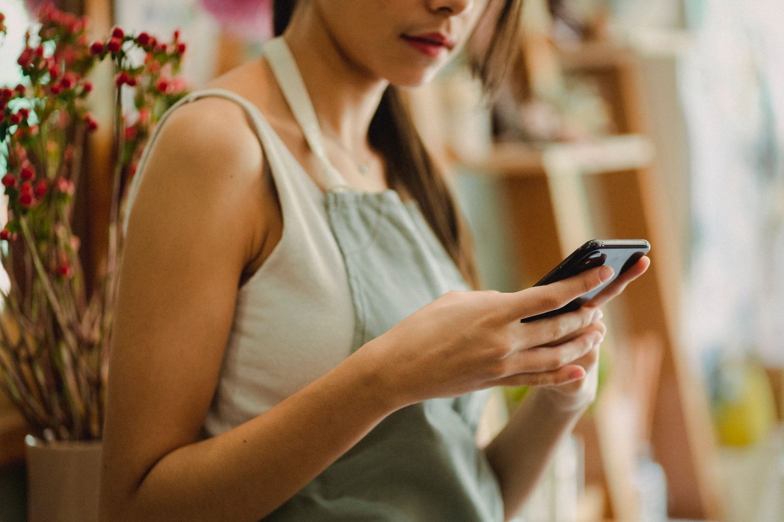 A florist in an apron checks her smartphone inside her flower shop.